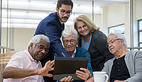 Vier ältere Menschen und ein Mann mittleren Alters schauen gemeinsam auf ein iPad